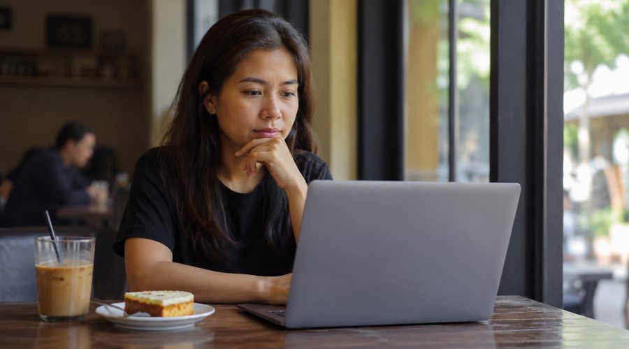 A woman researching on her laptop over iced coffee, weighing hiring a yaya directly versus going through an agency