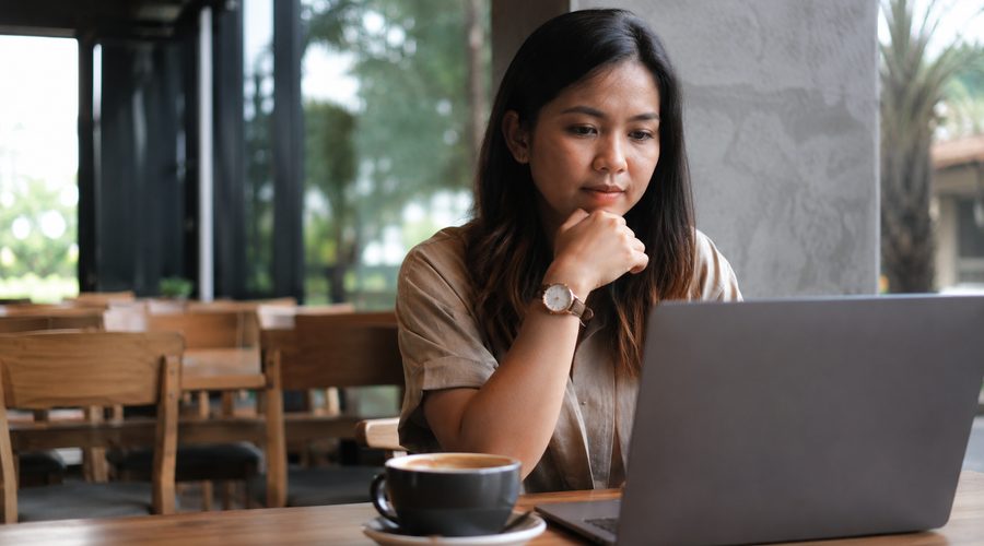 A Filipina helper working at a laptop in a bright cafe, writing up the profile families will read